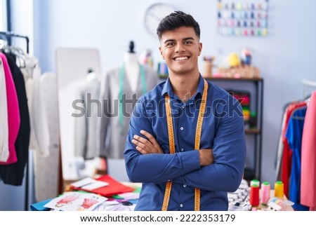 Young hispanic man tailor smiling confident standing with arms crossed gesture at clothing factory