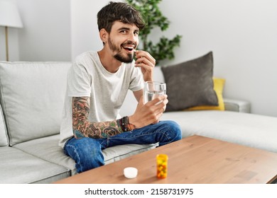 Young Hispanic Man Taking Pills Sitting On The Sofa At Home