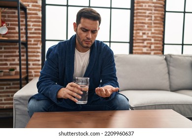 Young Hispanic Man Taking Pills Sitting On Sofa At Home