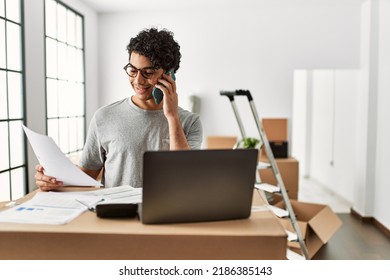 Young Hispanic Man Talking On The Smartphone Using Laptop At New Home.