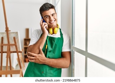 Young Hispanic Man Talking On The Smartphone Leaning On Window At Art Studio