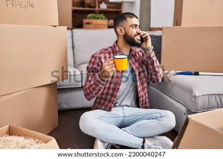 Young hispanic man talking on smartphone drinking coffee at new home