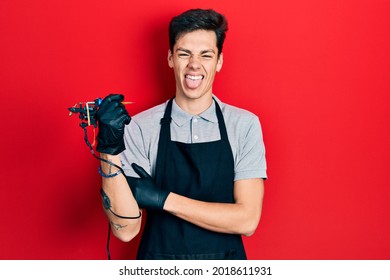 Young Hispanic Man Tattoo Artist Wearing Professional Uniform And Gloves Holding Tattooer Machine Doing Ok Sign With Fingers, Smiling Friendly Gesturing Excellent Symbol 