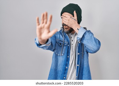 Young hispanic man with tattoos wearing wool cap covering eyes with hands and doing stop gesture with sad and fear expression. embarrassed and negative concept.  - Shutterstock ID 2285520203