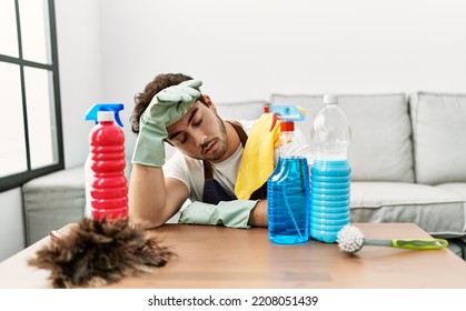 Young hispanic man tired leaning on table with cleaning products at home - Powered by Shutterstock