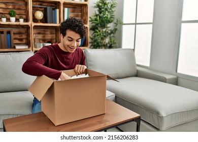 Young Hispanic Man Unboxing Cardboard Box Sitting On The Sofa At Home.