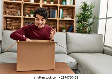 Young Hispanic Man Unboxing Cardboard Box Sitting On The Sofa At Home.