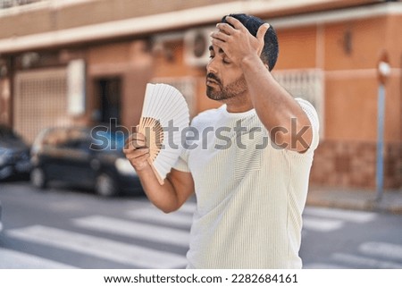 Young hispanic man using handfan sweating at street