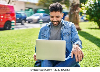 Young Hispanic Man Using Laptop Sitting On Herb At Park