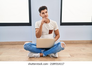 Young Hispanic Man Using Laptop At Home With Hand On Chin Thinking About Question, Pensive Expression. Smiling With Thoughtful Face. Doubt Concept. 