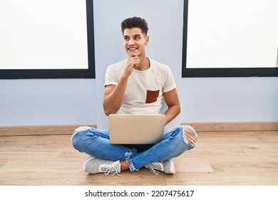 Young Hispanic Man Using Laptop At Home With Hand On Chin Thinking About Question, Pensive Expression. Smiling And Thoughtful Face. Doubt Concept. 