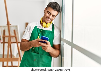 Young Hispanic Man Using Smartphone Leaning On Window At Art Studio