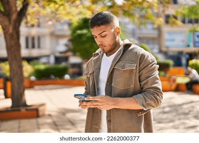 Young hispanic man using smartphone at park
