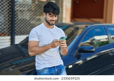 Young hispanic man using smartphone leaning on car at street