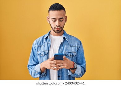 Young hispanic man using smartphone typing message relaxed with serious expression on face. simple and natural looking at the camera. 