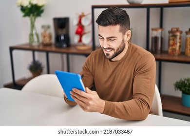 Young hispanic man using touchpad sitting on table at home