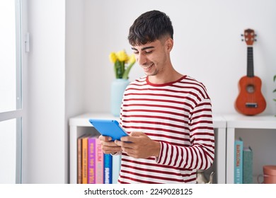 Young hispanic man using touchpad standing at bedroom