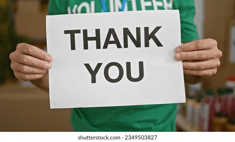 Young hispanic man volunteer holding thank you banner at charity center