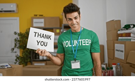 Young hispanic man volunteer holding thank you banner smiling at charity center