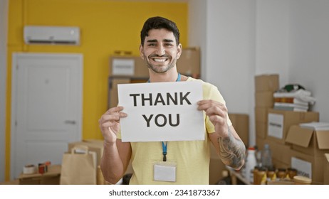 Young hispanic man volunteer smiling confident holding thank you banner at charity center