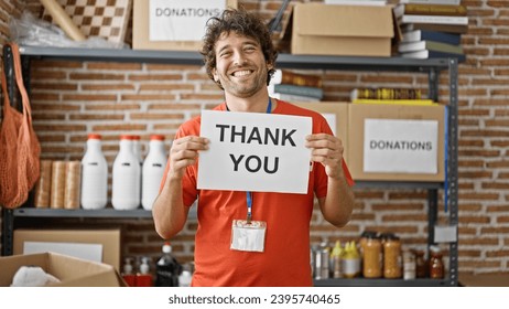 Young hispanic man volunteer smiling confident holding thank you banner at charity center