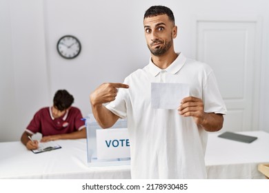 Young Hispanic Man Voting Putting Envelop In Ballot Box Pointing Finger To One Self Smiling Happy And Proud 