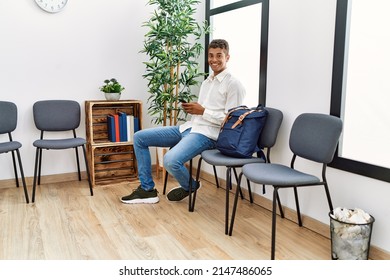 Young hispanic man waiting using smartphone at waiting room