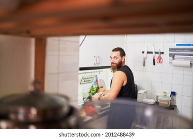 Young Hispanic Man Washing Dishes Looks At Camera. Everyday Chores