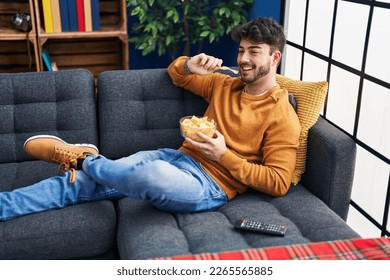 Young hispanic man watching movie sitting on sofa at home