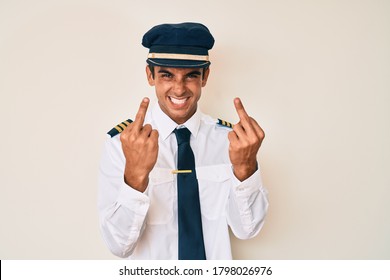 Young Hispanic Man Wearing Airplane Pilot Uniform Showing Middle Finger Doing Fuck You Bad Expression, Provocation And Rude Attitude. Screaming Excited 