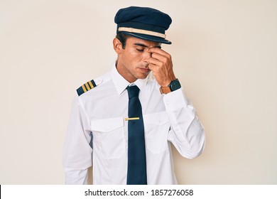 Young Hispanic Man Wearing Airplane Pilot Uniform Tired Rubbing Nose And Eyes Feeling Fatigue And Headache. Stress And Frustration Concept. 