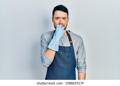 Young hispanic man wearing apron and gloves looking stressed and nervous with hands on mouth biting nails. anxiety problem.  - Powered by Shutterstock