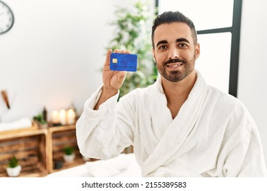 Young Hispanic Man Wearing Bathrobe Holding Credit Card At Beauty Center
