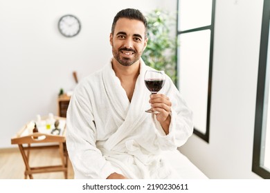Young Hispanic Man Wearing Bathrobe Toasting With Wine At Beauty Center