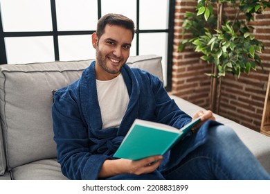 Young Hispanic Man Wearing Bathrobe Reading Book At Home