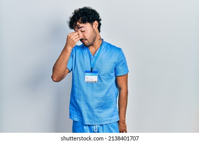 Young hispanic man wearing blue male nurse uniform tired rubbing nose and eyes feeling fatigue and headache. stress and frustration concept.  - Powered by Shutterstock