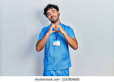 Young Hispanic Man Wearing Blue Male Nurse Uniform Smiling In Love Doing Heart Symbol Shape With Hands. Romantic Concept. 