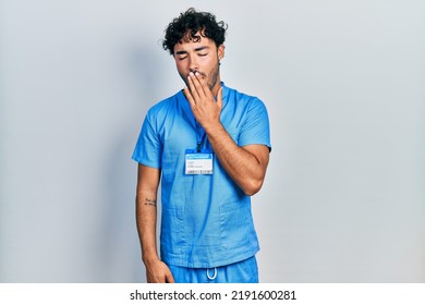 Young Hispanic Man Wearing Blue Male Nurse Uniform Bored Yawning Tired Covering Mouth With Hand. Restless And Sleepiness. 