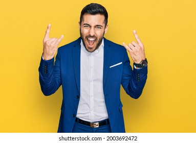 Young hispanic man wearing business jacket shouting with crazy expression doing rock symbol with hands up. music star. heavy music concept. 