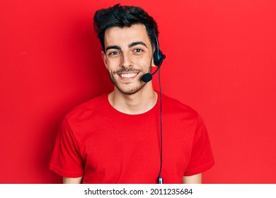 Young Hispanic Man Wearing Call Center Agent Headset Looking Positive And Happy Standing And Smiling With A Confident Smile Showing Teeth 