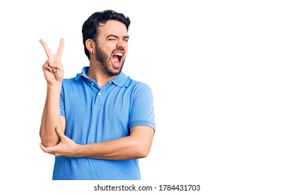 Young hispanic man wearing casual clothes smiling with happy face winking at the camera doing victory sign. number two.  - Shutterstock ID 1784431703