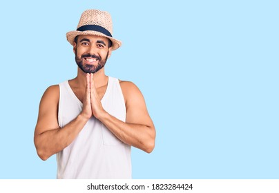 Young Hispanic Man Wearing Casual Summer Hat Praying With Hands Together Asking For Forgiveness Smiling Confident. 