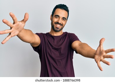 Young hispanic man wearing casual clothes looking at the camera smiling with open arms for hug. cheerful expression embracing happiness. 