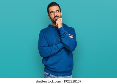 Young hispanic man wearing casual clothes serious face thinking about question with hand on chin, thoughtful about confusing idea 