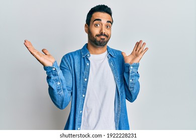 Young Hispanic Man Wearing Casual Clothes Clueless And Confused With Open Arms, No Idea And Doubtful Face. 