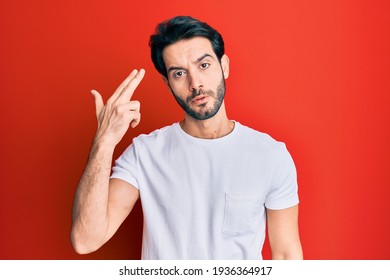 Young Hispanic Man Wearing Casual White Tshirt Shooting And Killing Oneself Pointing Hand And Fingers To Head Like Gun, Suicide Gesture. 