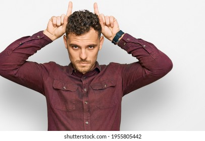Young Hispanic Man Wearing Casual Clothes Doing Funny Gesture With Finger Over Head As Bull Horns 