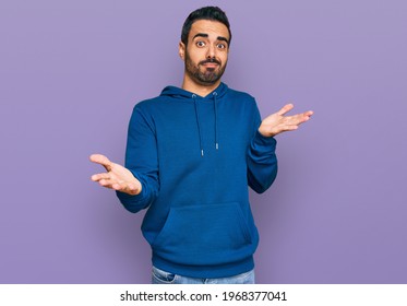 Young hispanic man wearing casual clothes clueless and confused expression with arms and hands raised. doubt concept. 