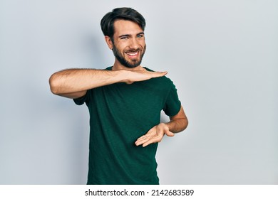 Young Hispanic Man Wearing Casual White Tshirt Gesturing With Hands Showing Big And Large Size Sign, Measure Symbol. Smiling Looking At The Camera. Measuring Concept. 