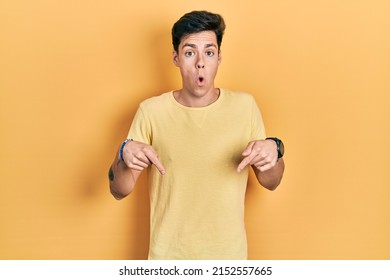 Young Hispanic Man Wearing Casual Yellow T Shirt Pointing Down With Fingers Showing Advertisement, Surprised Face And Open Mouth 